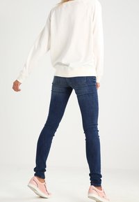 Weißes Sweatshirt mit gerippten Bündchen, kombiniert mit dunkelblauen Skinny-Jeans. Dazu passen hellrosa Sneaker für einen einfachen, lässigen Stil.