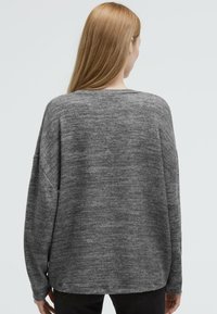 Grauer, übergroßer Pullover mit einer weichen, strukturierten Oberfläche, der einen weiten Halsausschnitt und abfallende Schulternähte aufweist, von hinten gezeigt.