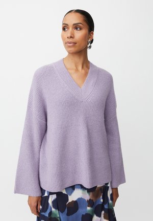 Lilac knit sweater with a V-neck, wide sleeves, and textured ribbing. Worn over a multi-colored floral skirt.