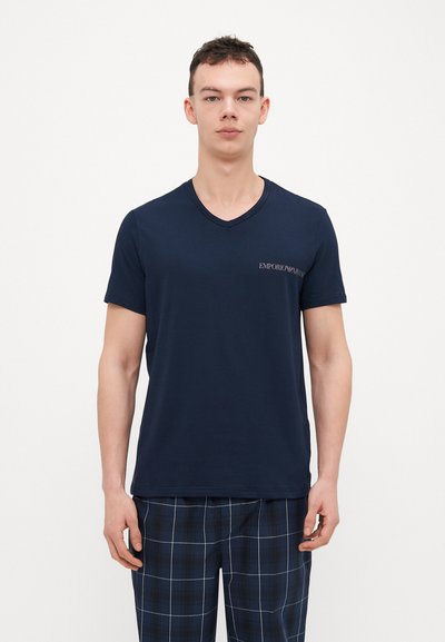 Námornícky modré tričko s V-výstrihom vyrobené z jemnej bavlny, s malým logom na ľavej hrudi. Model má na sebe kockované pyžamové nohavice.