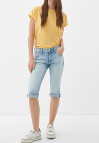 Camiseta amarilla de manga corta, jeans capri azul claro arremangados y zapatillas blancas. Tela suave, corte relajado y detalles mínimos.