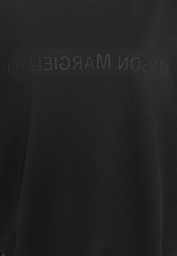 Černá mikina s měkkou texturou, s jemně vyraženým logem "MAISON MARGIELA" na přední straně. Jednoduchý, minimalistický design.