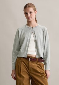 Ljusgrå cardigan med rund halsringning, knäppning fram och ribbad nederkant, bärs över en vit ribbad topp och är kombinerad med bruna kordfl collotranser.