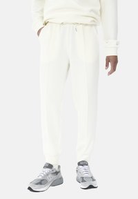 Hvide sweatpants med elastisk talje og snøre, der har sidelommer og en glat, blød tekstur. Kombineret med grå sneakers.