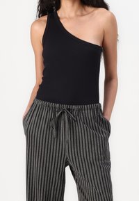 Bodysuit noir à une épaule en matière côtelée, associé  à un pantalon rayé gris et noir avec une taille élastique et un cordon de serrage.