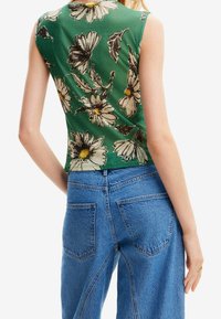 Vihreä ilmanhiha toppi, jossa on valkoisia ja ruskeita kukkakuviota, yhdistettynä korkeavyötäröisiin sinisiin farkkuihin, joissa on rento istuvuus.