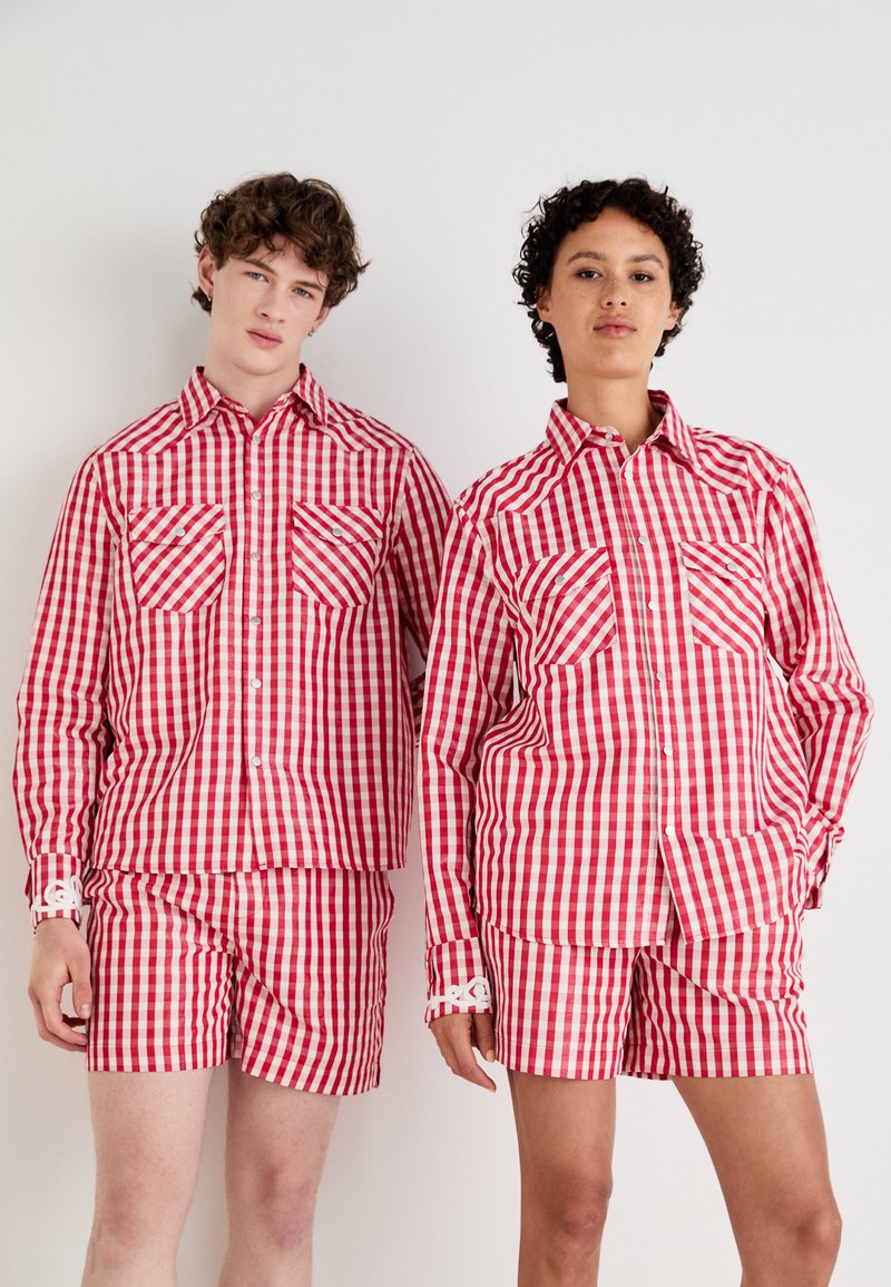 Rot-weiße karierte Hemden und Shorts mit klassischem Gingham-Muster, Knopfleiste und Brusttaschen, präsentiert von zwei Models.