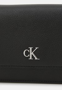 Portafoglio in pelle nera con superficie testurizzata, caratterizzato da un logo "cK" in argento e dettagli cuciti lungo i bordi.