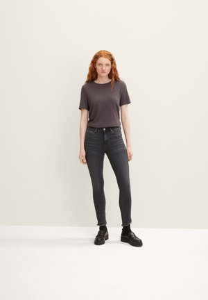 Grijze korte mouwen t-shirt gecombineerd met donkere skinny jeans en zwartleren instappers. De outfit heeft een minimalistisch ontwerp met een gladde textuur.