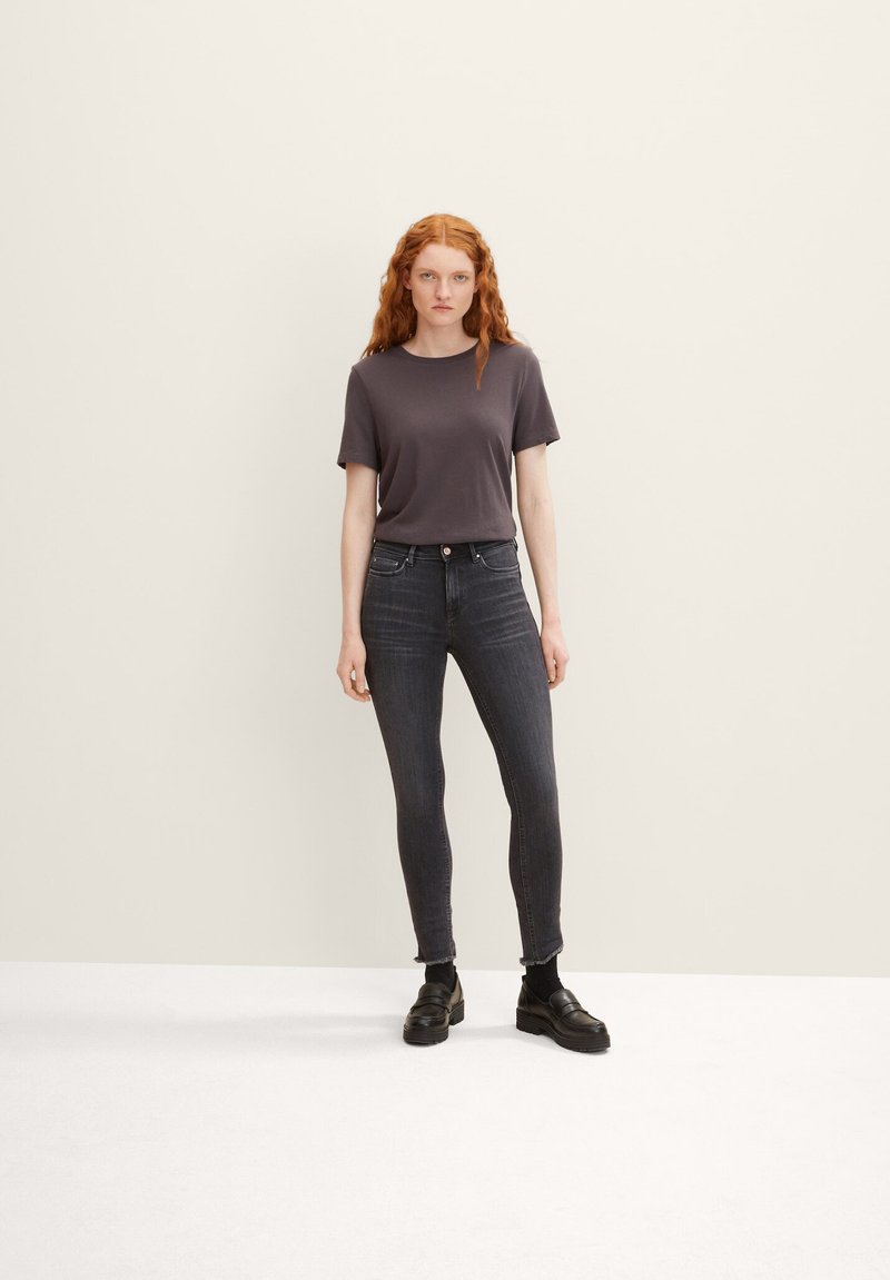 Grijze korte mouwen t-shirt gecombineerd met donkere skinny jeans en zwartleren instappers. De outfit heeft een minimalistisch ontwerp met een gladde textuur.