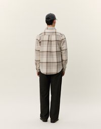 Kariertes Flanellhemd in Beige und Braun mit abgerundetem Saum und Knopfleiste. Kombiniert mit einer dunklen, lockeren Hose.