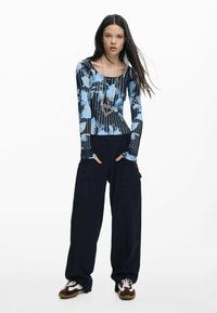 Bluză cu mâneci lungi, de culoare albastră, cu modele abstracte, asortată cu pantaloni cargo negri largi și adidași maro cu alb. Accesoriu colier argintiu cu inimă.