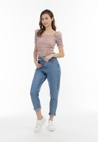 Top corto con stampa floreale e maniche a sbuffo, abbinato a jeans a vita alta blu chiaro e sneakers bianche. Tessuto morbido e vestibilità aderente.