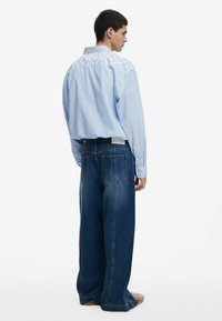 Gestreiftes blaues Hemd mit einem großen weißen bestickten Rückendesign, kombiniert mit übergroßen blauen Jeans aus Denim mit zwei Gesäßtaschen.