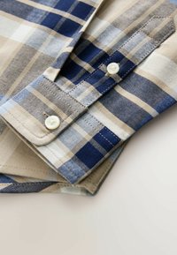 Camisa de algodón a cuadros con tonos beige claro, azul marino y azul. Cuello abotonado con botones blancos y textura suave.