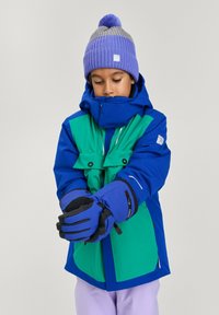 Niebieska i zielona wodoodporna kurtka z wysokim kołnierzem, dwoma kieszeniami na piersi i odblaskowymi akcentami. Niebieskie rękawice i dzianinowa fioletowa czapka.
