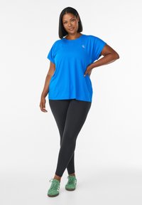Blaues Kurzarm-Sportoberteil mit Rundhalsausschnitt, kombiniert mit schwarzen Leggings und grünen Sportschuhen; glattes Material mit lockerer Passform.