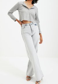 Graues, tailliertes Langarmoberteil mit Kragen und Knöpfen, kombiniert mit hochgeschnittenen, hellblauen, weit geschnittenen Jeans und grauen Absatzsandalen.