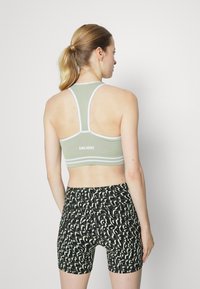 Sutiã desportivo verde com detalhes brancos e design de costas nadador, combinado com calções pretos que apresentam um padrão abstrato em verde claro.