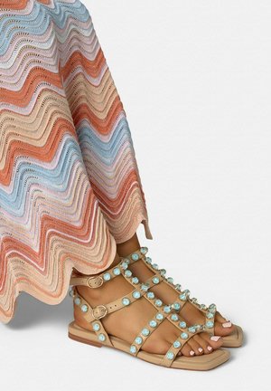 Sandalias planas beige con tiras de piedras azules, usadas con una falda multicolor de crochet con patrón de olas.