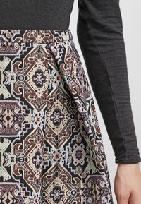 Gonna patterned con design geometrici in tonalità marrone, nero e pastello. Realizzata in tessuto testurizzato con un dettaglio di piega laterale.