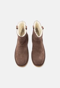 Botas de tornozelo em camurça castanha com forro de pelúcia creme, abas de puxar nas laterais e solas de borracha costuradas, vistas de cima sobre fundo branco.