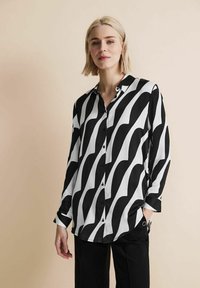 Camicia a maniche lunghe bianco e nero con motivo a onde, chiusura con bottoni, colletto e vestibilità rilassata, abbinata a pantaloni neri.