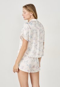 Korte mouwen, lichtgewicht pyjama set in zachte stof, met een pastel patroon van katten en linten in roze en blauw op een crèmekleurige achtergrond.