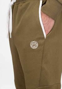 Olivgrüne Jogginghosen aus Baumwollmischung, mit weißen Kordeln, seitlichen Taschen und einem runden gestickten Logo am Oberschenkel.