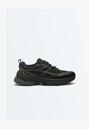 Čierna robustná teniska s hrubou podrážkou, sieťovinovým a syntetickým zvrškom, polstrovaným golierom, šnurovaním vpredu a sťahovacou slučkou na päte, zobrazená z bočného pohľadu.