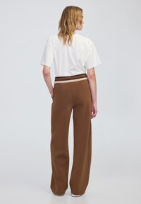 Brązowe spodnie o szerokich nogawkach z teksturowanym wykończeniem i kontrastującym paskiem w paski. Połączone z luźną białą koszulką.