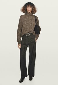 Hnědý pletený svetr s vysokým límcem, kombinovaný s tmavými volnými kalhotami a černými kotníkovými botami. Obsahuje malou černou tašku.