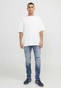 Camiseta blanca de algodón de manga corta, combinada con jeans claros desgastados con roturas. Zapatillas oscuras con acentos blancos.