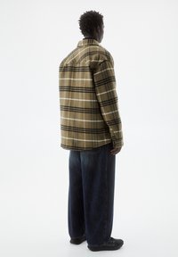 Camisa de franela a cuadros marrón con rayas negras y blancas, con un corte relajado y cuello abotonado, combinada con unos vaqueros holgados de mezclilla oscura.