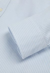 Manga de camisa de dress azul claro con rayas verticales blancas, puño abotonado y parte del cuerpo de la camisa con el mismo patrón.