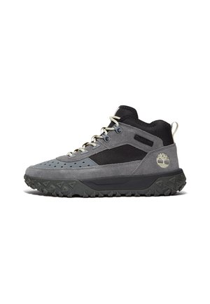 Scarponcino da trekking di media altezza grigio e nero con suola nera testurizzata, chiusura anteriore con lacci, linguetta sul tallone e logo dell'albero Timberland sul lato esterno.