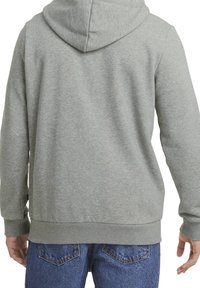 Felpa grigia con una texture morbida, dotata di un grande cappuccio, polsini e orlo a coste. Il design sul retro è semplice e privo di dettagli aggiuntivi.