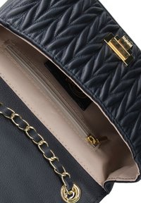 Borsa a tracolla in pelle nera trapuntata con hardware oro, dotata di un compartimento con zip e una tracolla con catena, all'interno beige liscio.