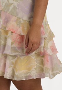 Blomstrete kjole med lagdelte volanger. Laget av lett stoff i pastellfarger: rosa, gul og grønn. Hånd synlig ved kanten.