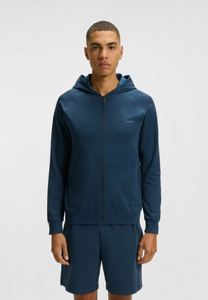 Marineblauer Reißverschluss-Hoodie mit Kapuze, ausgestattet mit einer Fronttasche und einem Logo auf der Brust. Hergestellt aus einem glatten, leichten Stoff.