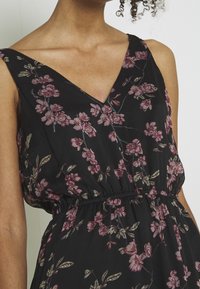 Blommig klänning med svart bakgrund, v-ringning och elastisk midja. Tyget är lätt och flödande med rosa blommor och gröna blad.