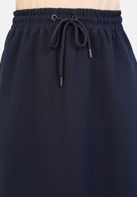 Tmavě modrá sukni s elastickým pasem a šňůrkou. Má hladkou texturu a minimalistický design, vhodná pro volný čas.