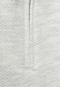 Tejido blanco texturizado que muestra un patrón de espiga con un sutil brillo. Presenta un detalle de costura limpio para un diseño estructural.