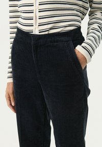 Marineblauwe corduroy broek met verticale ribbels, voorzien van zijzakken en een zachte, gestructureerde afwerking, gecombineerd met een wit en marineblauw gestreept shirt.