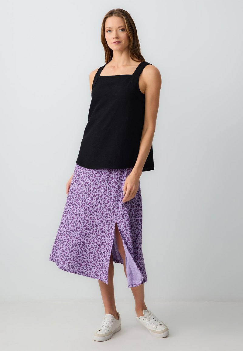 Top nero senza maniche con scollo a quadrato abbinato a una gonna floreale lilla con uno spacco alto fino alla coscia. Sneakers bianche completano il look.