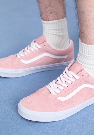 Person iført hvide sokker og pink lave sneakers med hvide snørebånd på et lyseblåt tæppe.