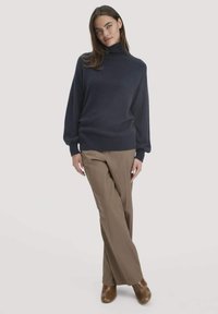 Marineblauer Rollkragenpullover mit langen Ärmeln, lockerer Passform und geripptem Saum, kombiniert mit beigen weit geschnittenen Hosen und braunem Schuhwerk.