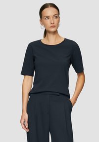 Navyblaues T-Shirt mit kurzen Ärmeln aus weichem Baumwollmischgewebe, mit rundem Ausschnitt und lässiger Passform. Getragen mit maßgeschneiderten dunklen Hosen.