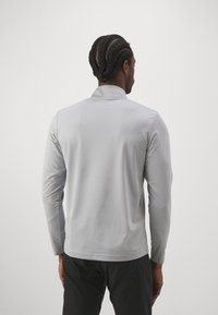 Lys grå langermet polo med en subtil teksturert mønster, stående krage og rett kant, brukt med mørke bukser.