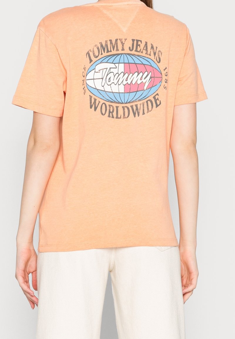 Kortärmad orange T-shirt med "Tommy Jeans Worldwide" grafik i blått och rosa på baksidan; mjukt tyg och avslappnad passform.